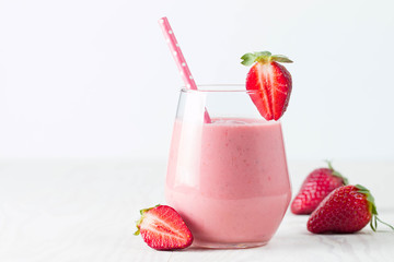 Glass of fresh strawberry milkshake, smoothie and fresh strawberries on pink, white and wooden...