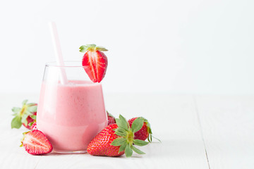 Glass of fresh strawberry milkshake, smoothie and fresh strawberries on pink, white and wooden background. Healthy food and drink concept.