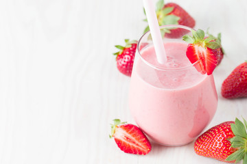 Glass of fresh strawberry milkshake, smoothie and fresh strawberries on pink, white and wooden background. Healthy food and drink concept.