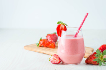 Glass of fresh strawberry milkshake, smoothie and fresh strawberries on pink, white and wooden background. Healthy food and drink concept.