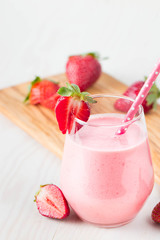 Glass of fresh strawberry milkshake, smoothie and fresh strawberries on pink, white and wooden background. Healthy food and drink concept.