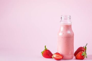 Glass of fresh strawberry milkshake, smoothie and fresh strawberries on pink, white and wooden background. Healthy food and drink concept.