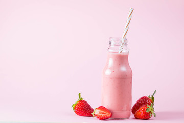 Glass of fresh strawberry milkshake, smoothie and fresh strawberries on pink, white and wooden background. Healthy food and drink concept.