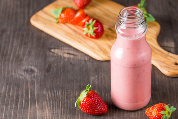 Glass of fresh strawberry milkshake, smoothie and fresh strawberries on pink, white and wooden background. Healthy food and drink concept.