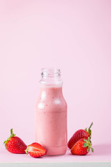 Glass of fresh strawberry milkshake, smoothie and fresh strawberries on pink, white and wooden background. Healthy food and drink concept.