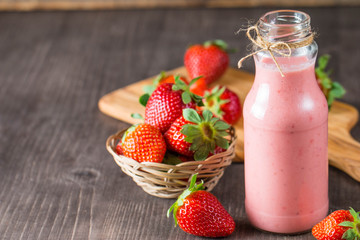 Glass of fresh strawberry milkshake, smoothie and fresh strawberries on pink, white and wooden background. Healthy food and drink concept.
