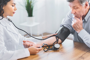 Female doctor checking blood pressure of senior man