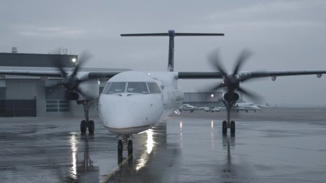 Propeller plane arrives at airport and moves across wet icy tarmac arrival at gate