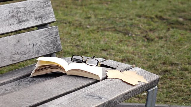 Wind moving the pages of a book lying on a wooden park bench