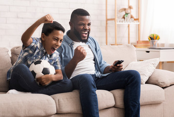 Black father and son soccer fans watching football on tv