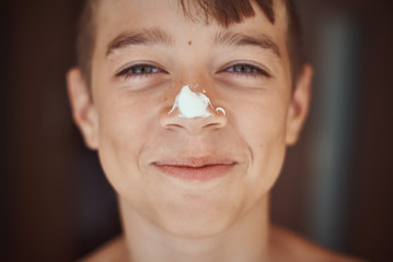Happy smile boy with sunscreen cream on the nose, close up portrait. Summer holidays and vacation...