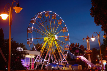 Illuminated ferris wheel in amusement park at a night city