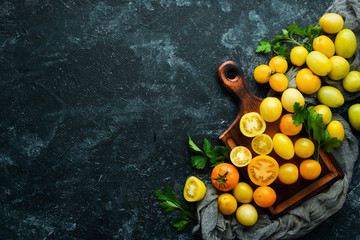 Yellow tomatoes on black stone background. Top view. Free space for your text.