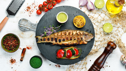 Grilled trout with vegetables on a black plate. Top view. free space for your text. Rustic style.