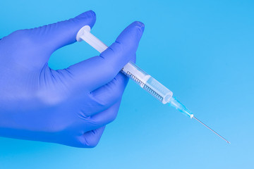 Hand in a medical glove with a syringe on a blue background. Close-up. Vaccinations. Medicine....