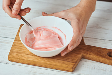 Woman whisking red cream for decorating cookies in a bowl on kitchen, closeup