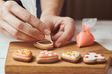 Decorating gingerbread cookies with icing. Woman hand decorate cookies in shape of heart, closeup