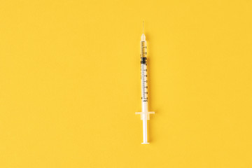 Medical syringe on the yellow background, top view with copy space. Vaccination and virus...