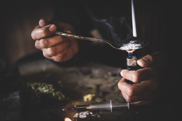 Drug addicts in the dark room. Addict/junkie preparing drugs with a spoon and lighter. White powder and a syringe. Drug concept. International drug abuse day. - obrazy, fototapety, plakaty
