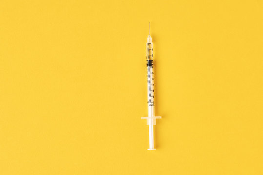 Medical syringe on the yellow background, top view with copy space. Vaccination and virus protection concept