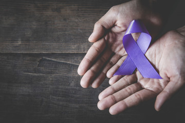 Purple ribbon in a woman's hand, Domestic Violence Awareness Month (October) concept with deep purple awareness ribbon.