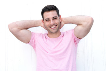 Close up handsome young man smiling with hands behind head by white background