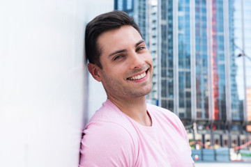 Close up smiling handsome young man leaning against white wall in city