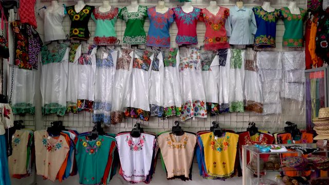 Camera pans down in a store display of women’s Mexican ethnic blouses and dresses in a shop in Merida, Mexico.