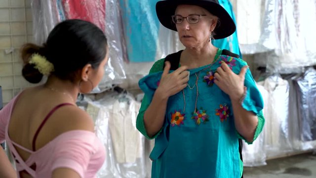 Mature woman holds a Mexican huipil blouse up to her looking for good fit in a store in Merida, Mexico.