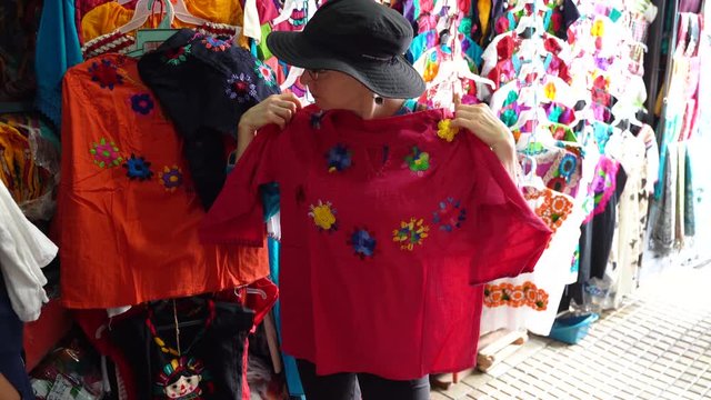 Mature woman tourist holds up a pink huipil blouse and then looks in a mirror in a store in Merida, Mexico.