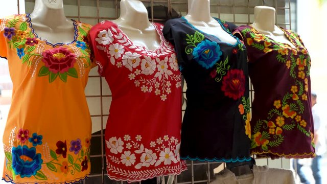 Camera turns to left as it moves right showing huipil Mexican blouses for women in a shop in Merida, Mexico.