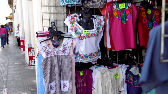 Camera pushes in and rotates showing Mexican blouses for women in a store in Merida, Mexico.