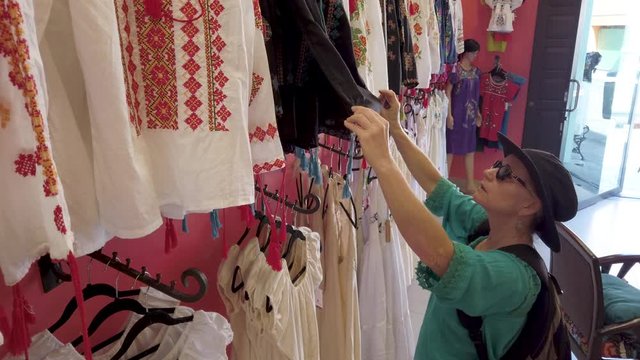 Mature woman looks at a beautiful display of women’s huipil blouses in Merida Mexico store.