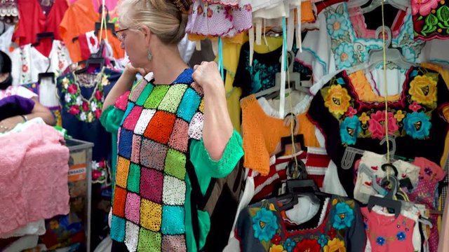 Mature woman holds up colorful mexican crocheted blouse and asks, do you like it and smiles in Merida, Mexico.