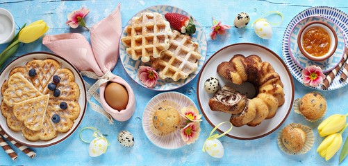 Easter festive dessert table with various of cakes, waffles, sweets and strawberry. Blue...