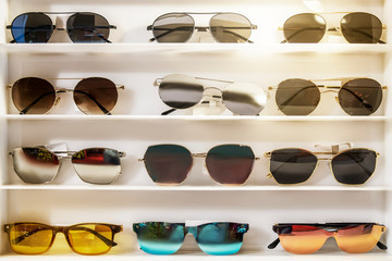 Sunglasses of different colors on the store white counter. beautiful and bright, selection and...