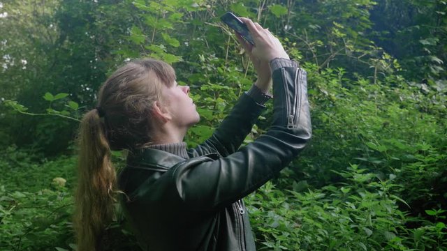 Young adult female takes photos with smartphone in forest, medium