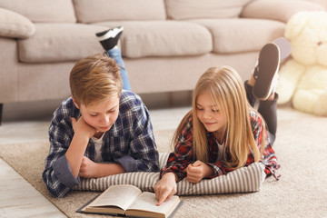 Brother And Sister Reading Book Lying On Floor At Home