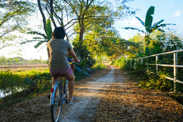 Baby boy ride bicycle with mother in rural road tree forest sunset light