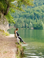 Beautiful, cute pregnant woman sits near a mountain lake in a forest on the shore