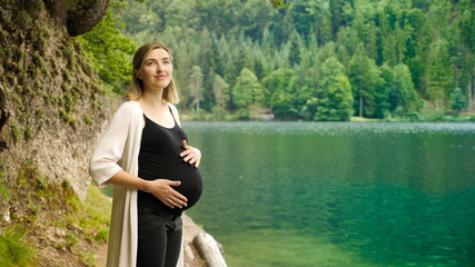 Beautiful pregnant woman near a mountain lake in the forest.