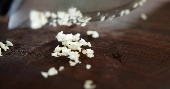 closeup of chef knife mincing garlic and gathering it on the table