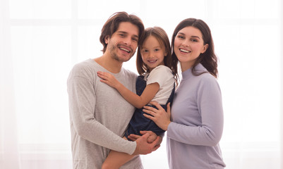 Fototapeta premium Smiling Parents Holding Little Daugher In Arms And Posing At Camera