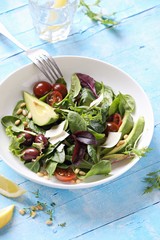 Green salad with avocado, tomatoes, olives and parmesan. Light blue background
