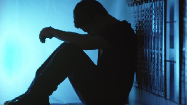 Troubled Teen Sitting in School Hallway Against Lockers