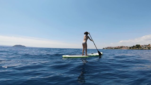 Young woman doing stand up paddling on a turquoise water. Outdoor sport activities in Greece on a sunny day.