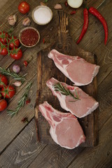 raw pork loin or sliced meat isolated on a wooden cutting board and tomatoes and spices on a rustic wooden background. Flat lay. Top view. Vertical photo.