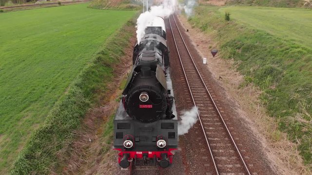 Aerial pushback view Historic locomotive steam train crossing green fields, steam smoke