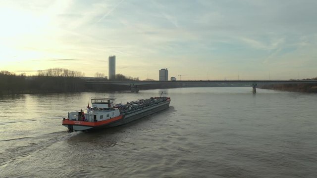 Cinematic drone / aerial shot of a ship on the river rhine in bonn with the post tower and the konrad-adenauer bridge at the golden hour, 30p