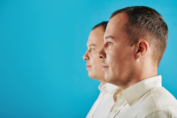 Fototapeta premium Caucasian man wearing white shirt standing with his twin brother looking at something, conceptual side view shot